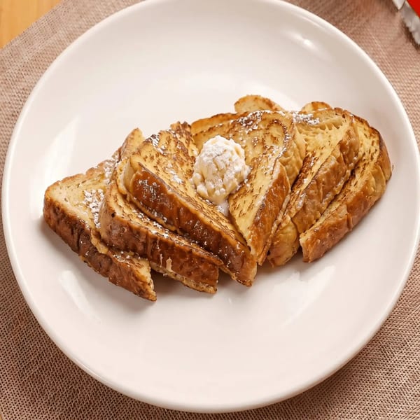 Golden French toast slices, dusted with powdered sugar and topped with a dollop of cream, on a white plate.