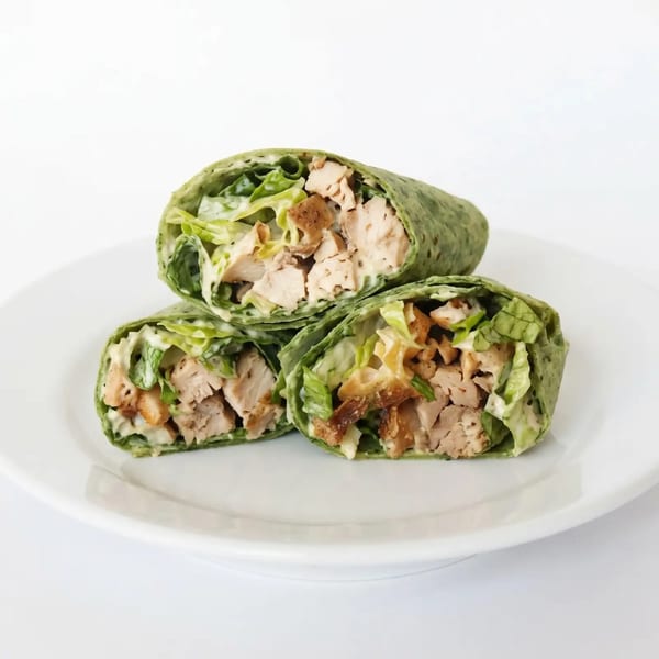 Three chicken Caesar salad wraps with green tortillas, lettuce, and chicken on a white plate.